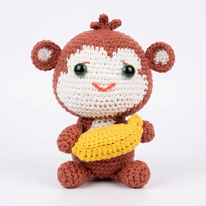 Crocheted monkey toy with a banana on a white background